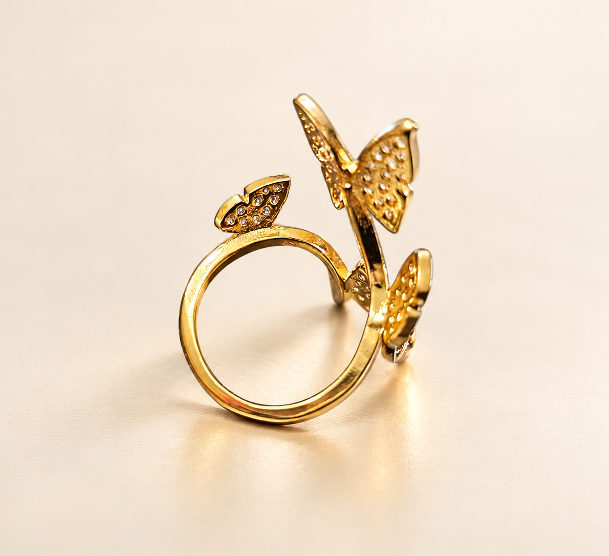 Bague Envol aux Papillons Dorés — Bague vue de trois-quarts sur fond crème, anneau circulaire au premier plan et trois papillons dorés en relief à différentes hauteurs.