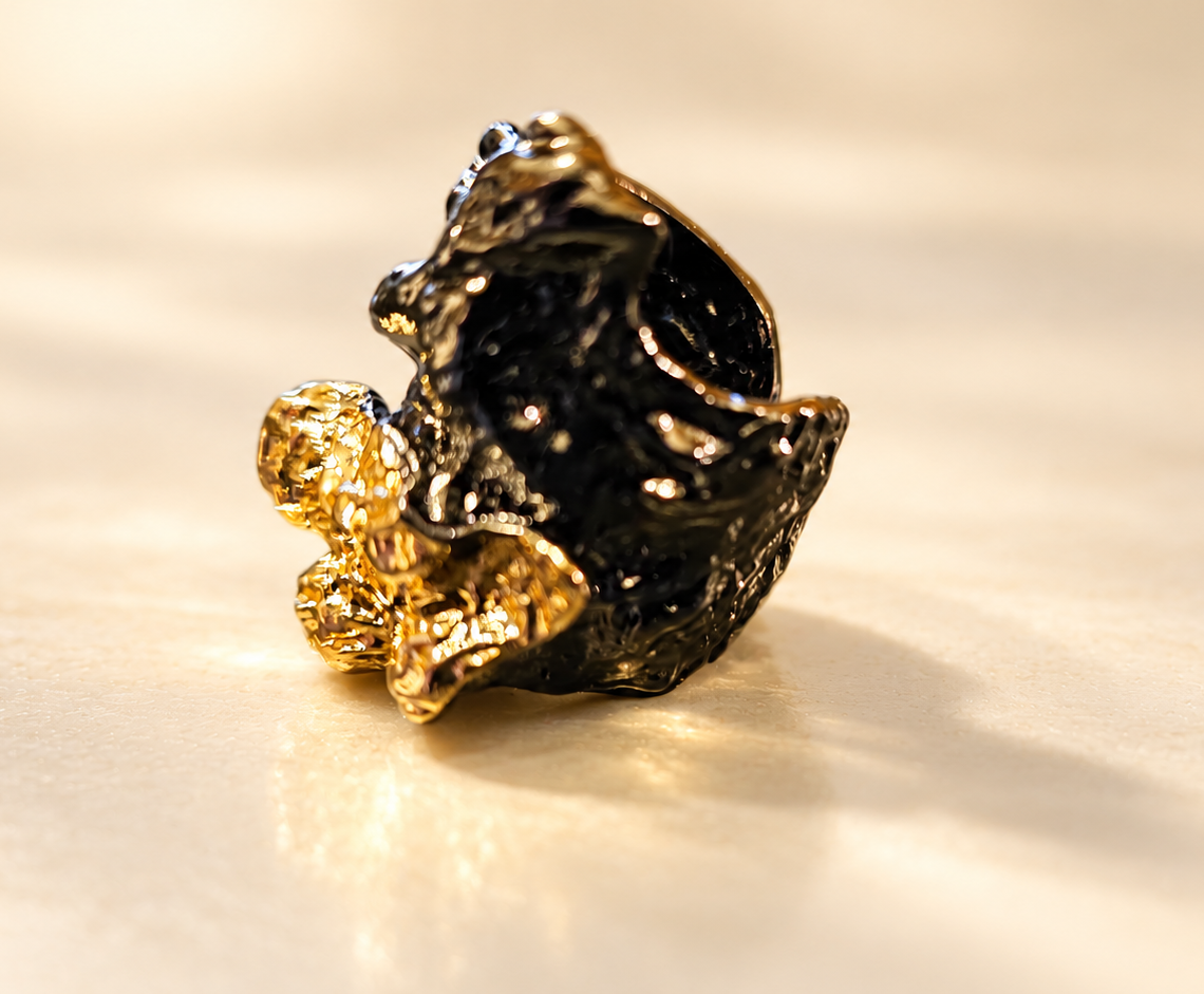 Bague Tellure Relief Noir & Doré — Bague seule sur fond clair, vue de trois-quarts, avec surface noire creusée, contours ondulés et reliefs dorés brillants au premier plan.