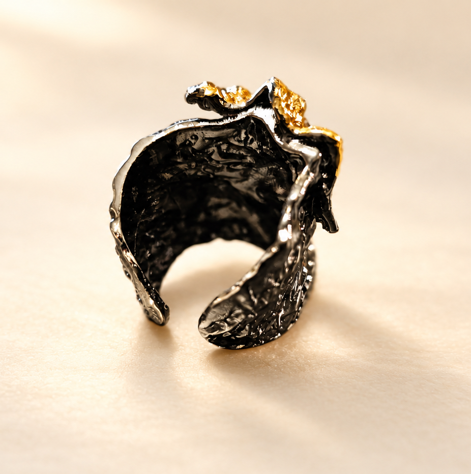 Bague Tellure Relief Noir & Doré — Bague large vue de biais par l’intérieur, anneau ouvert noir brillant, texture irrégulière et reliefs dorés sur le haut, sur fond clair.