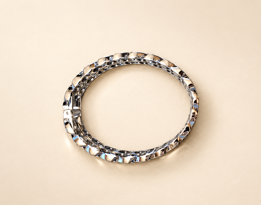 Bracelet Manchette Entrelacs Argentés — Bracelet argenté posé à plat sur fond clair, contour arrondi à reliefs entrecroisés et mécanisme à ressort visible à gauche.