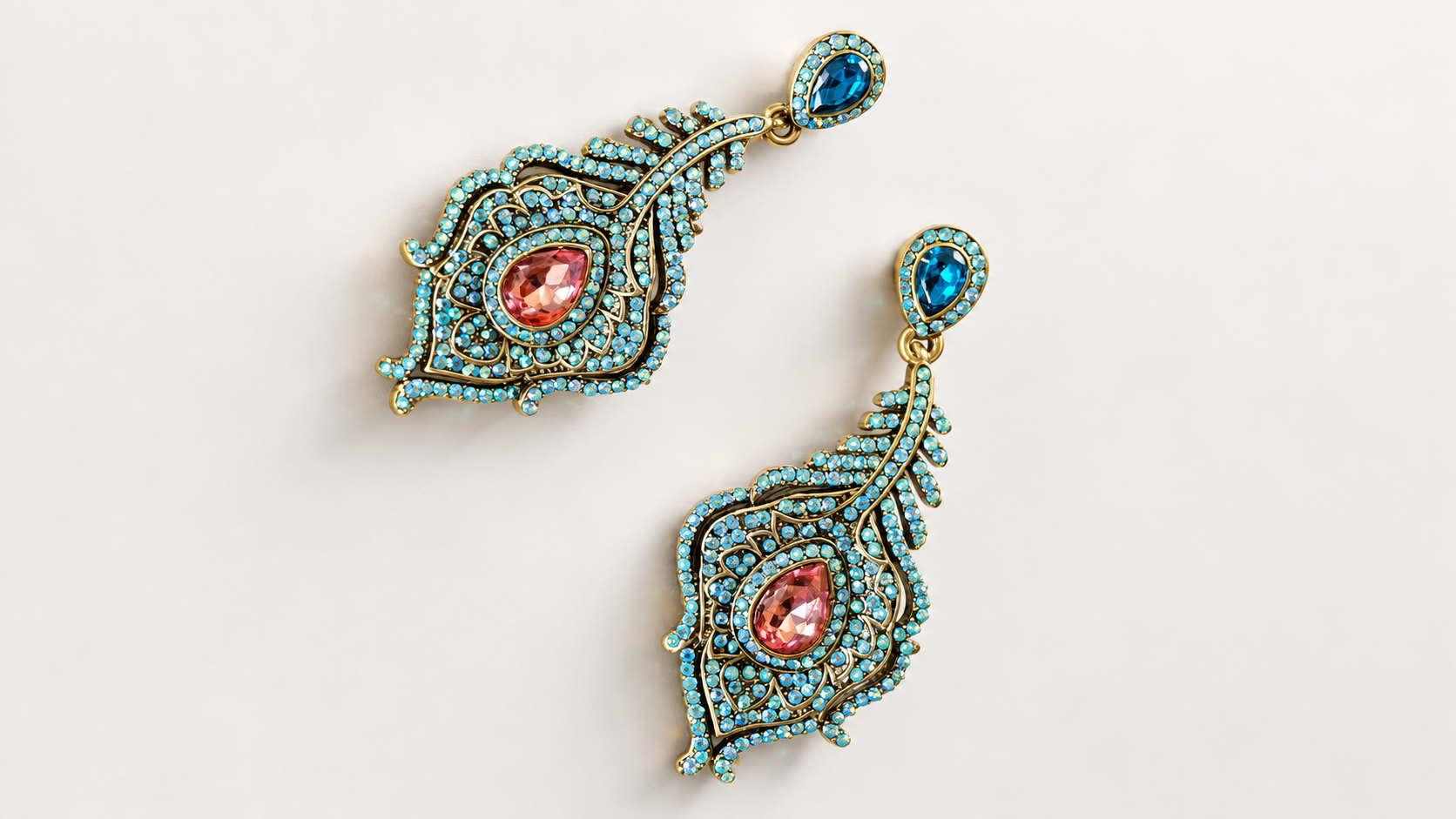 Boucles d’oreilles Parade Plumes Bleues & Roses — Deux boucles disposées en diagonale sur fond clair, motifs plumes ajourés dorés, petits éléments bleu-vert et gouttes facettées bleues et roses.
