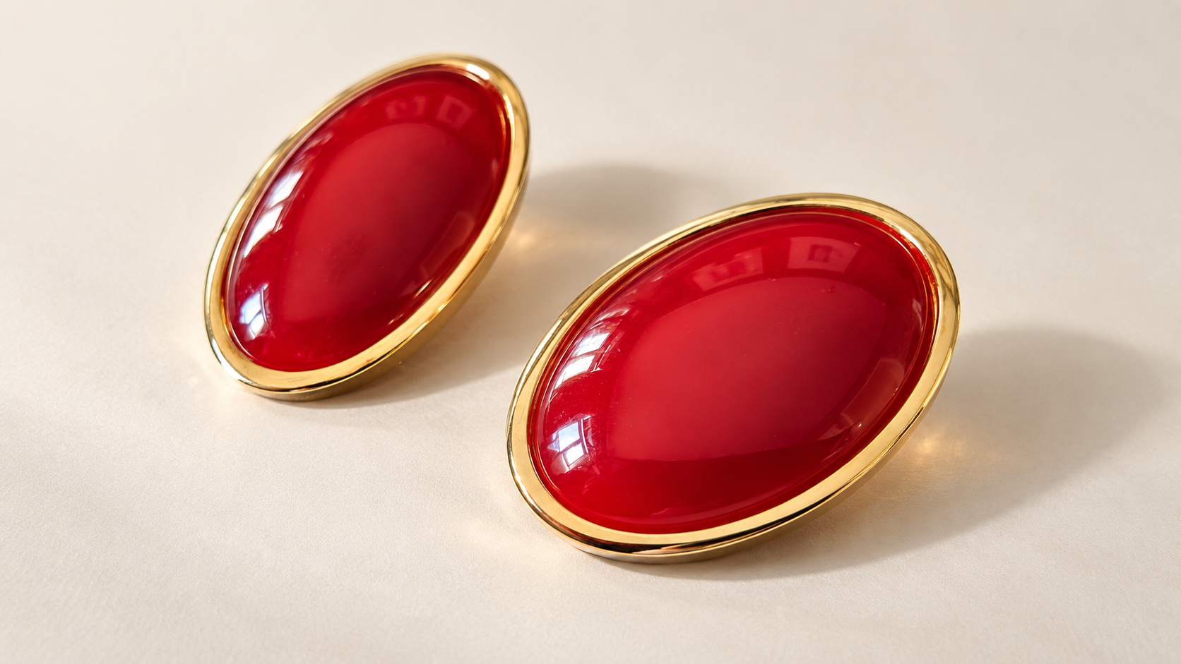 Boucles d’oreilles Flamme Ovales Rouges & Doré — Deux boucles ovales disposées en diagonale sur fond clair, cabochons rouges brillants entourés de contours dorés.