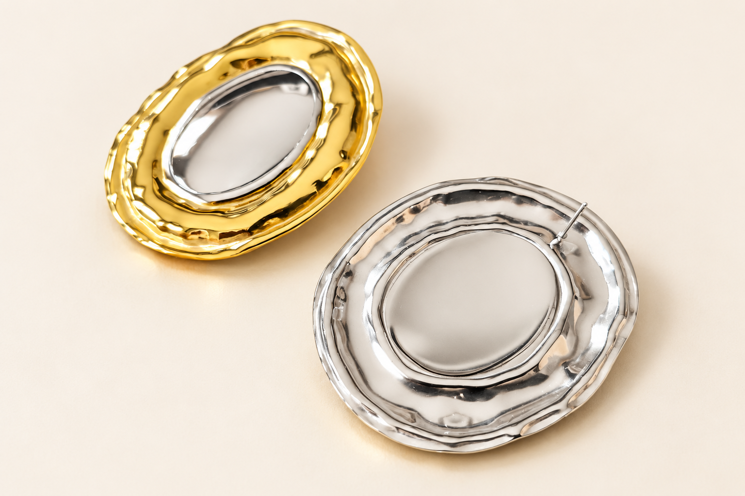 Boucles d’oreilles Halo Ovale Bicolore — Deux boucles ovales ajourées sur fond clair, l’une montrant sa face dorée au bord intérieur argenté, l’autre son dos argenté avec une tige visible.