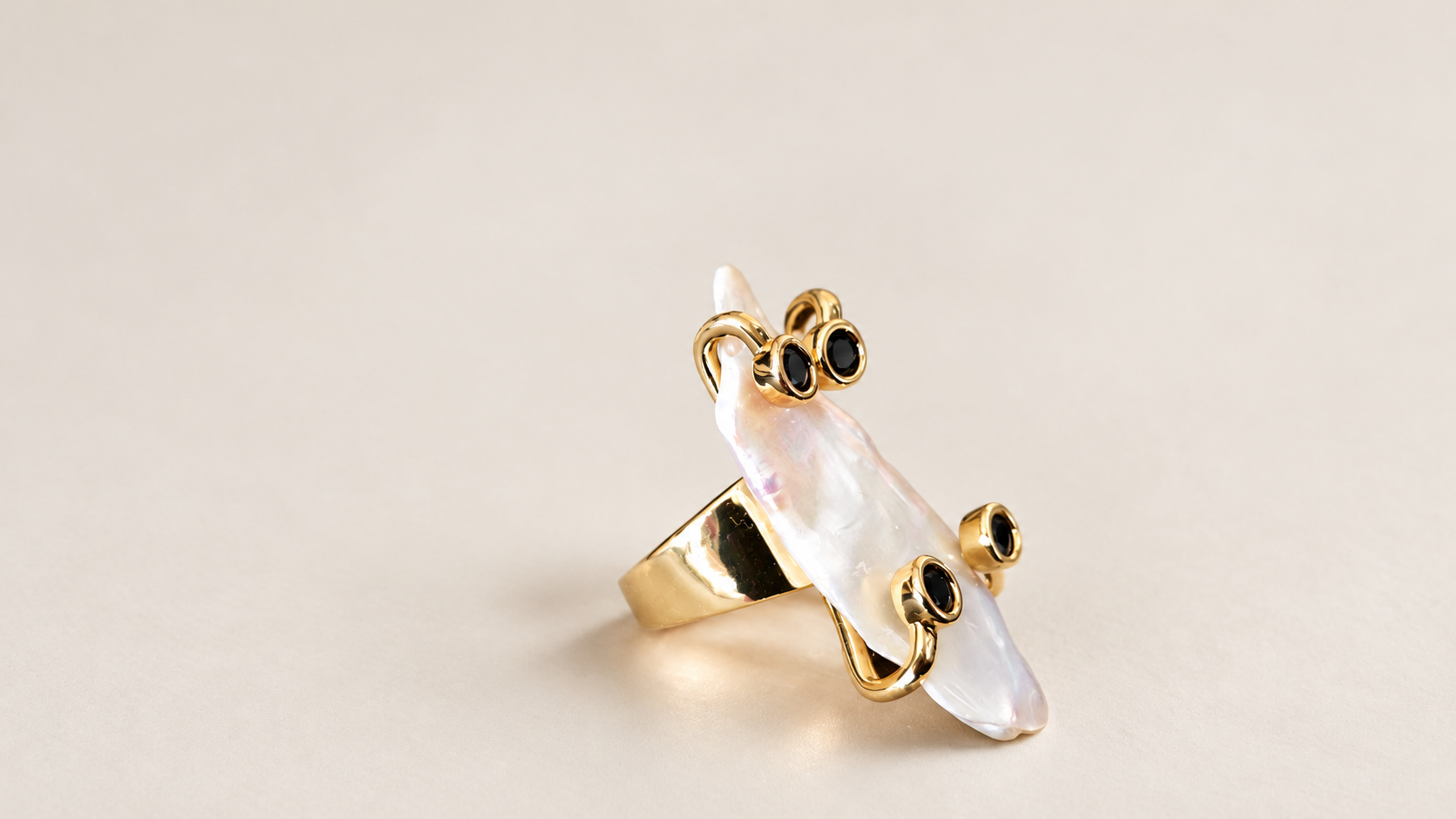 Bague Silhouette Irisée & Accents Noirs — Bague de trois-quarts avec anneau large visible à gauche, centre blanc à reflets rosés et détails noirs en relief.