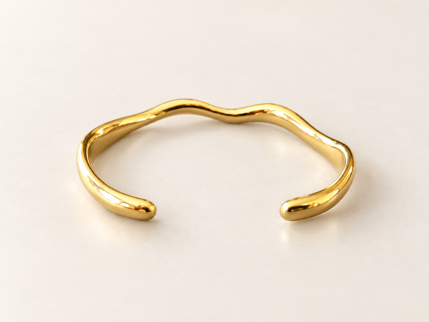 Bracelet Jonc Sillage Doré — Intérieur du jonc doré visible, deux extrémités arrondies au premier plan et contour ondulant à l’arrière.