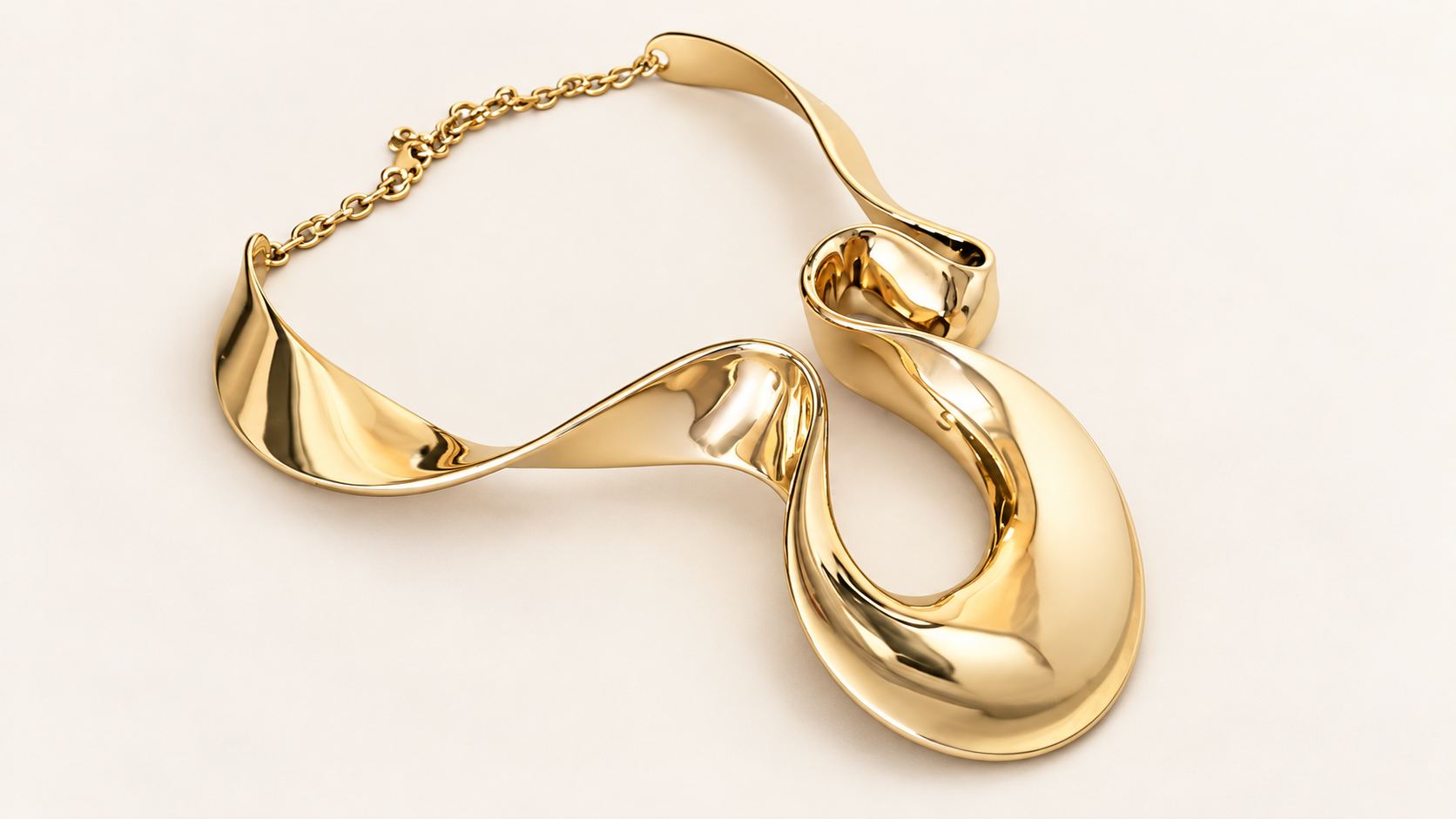 Parure Arabesque — Collier doré vu en biais, avec les creux du ruban ondulé, une large boucle au premier plan et la chaîne en arrière.