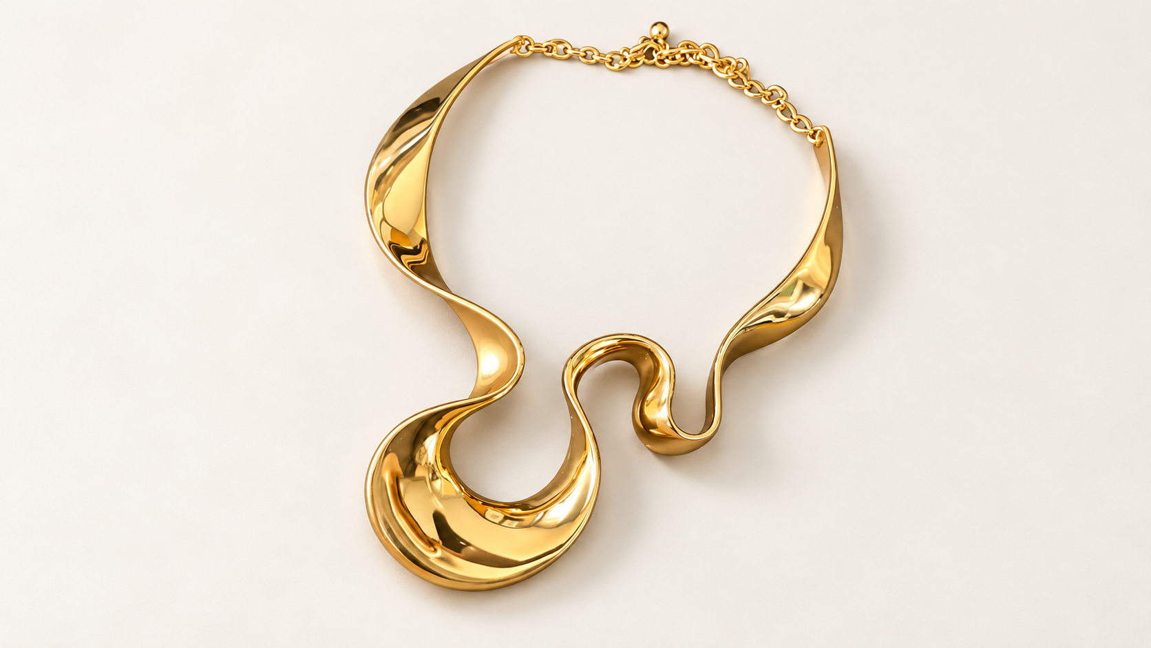 Parure Arabesque — Collier seul posé à plat, montrant ses courbes dorées brillantes, sa grande boucle décentrée et sa chaîne arrière.