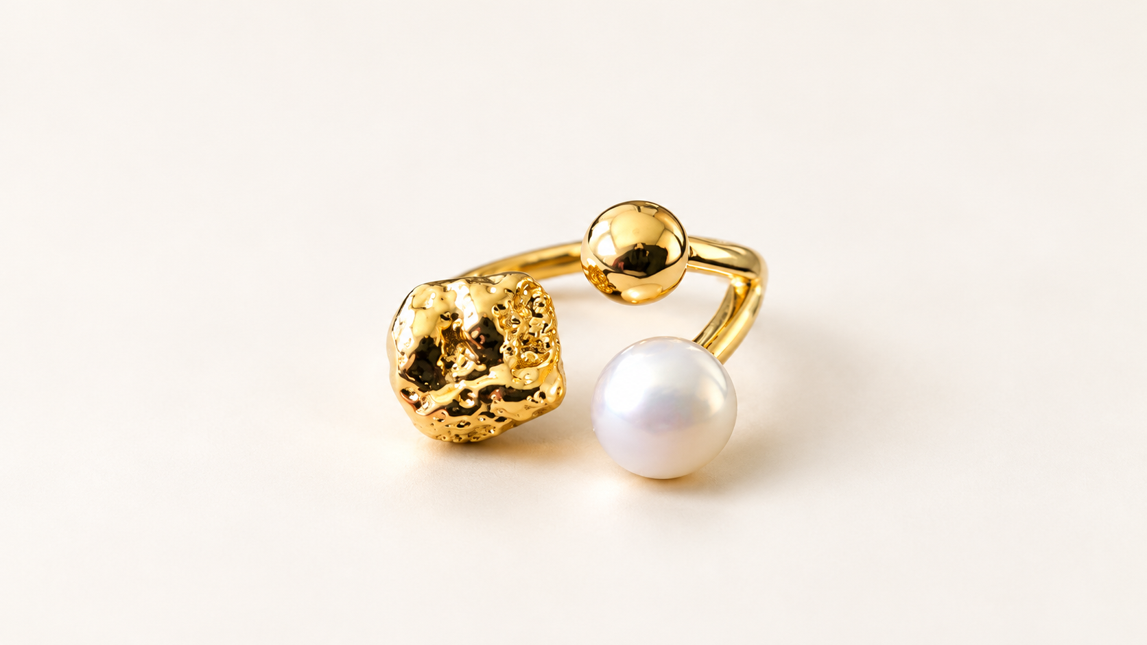Parure Arabesque — Gros plan du décor de la bague : élément doré irrégulier, boule dorée lisse et boule blanche aux reflets perlés.