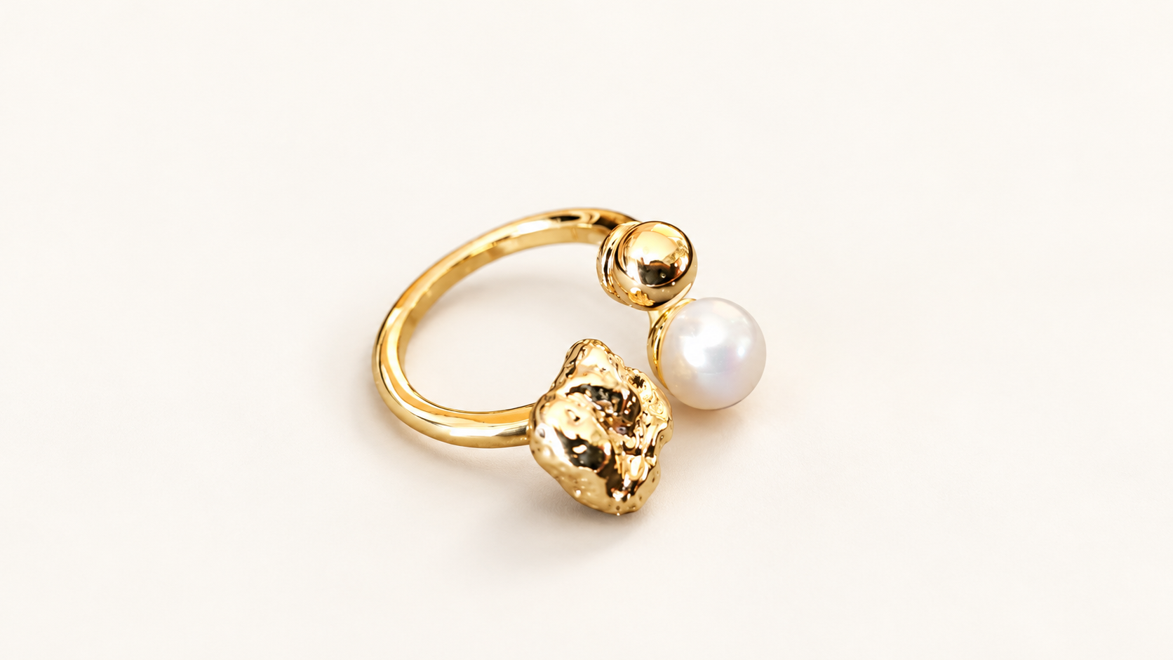 Parure Arabesque — Bague dorée vue de dessus, avec anneau ouvert et trois éléments décoratifs regroupés sur l’avant, dont une boule blanche.