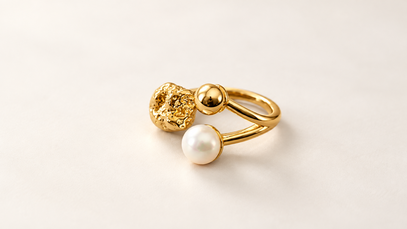 Parure Arabesque — Bague vue de trois-quarts, montrant ses lignes dorées dédoublées, son relief irrégulier et ses deux boules lisses, dorée et blanche.