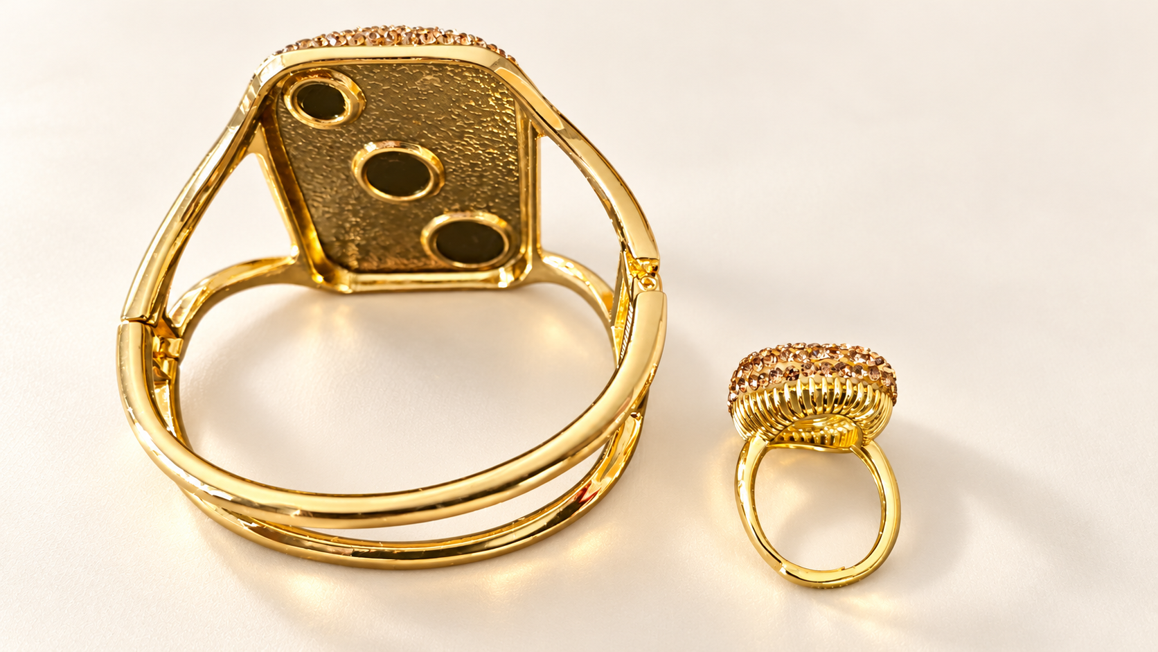 Parure Incandescence Rouge — Dos doré du bracelet avec trois ouvertures circulaires et double ligne arrondie ; arrière de la bague montrant l’anneau ouvert et la monture ajourée.