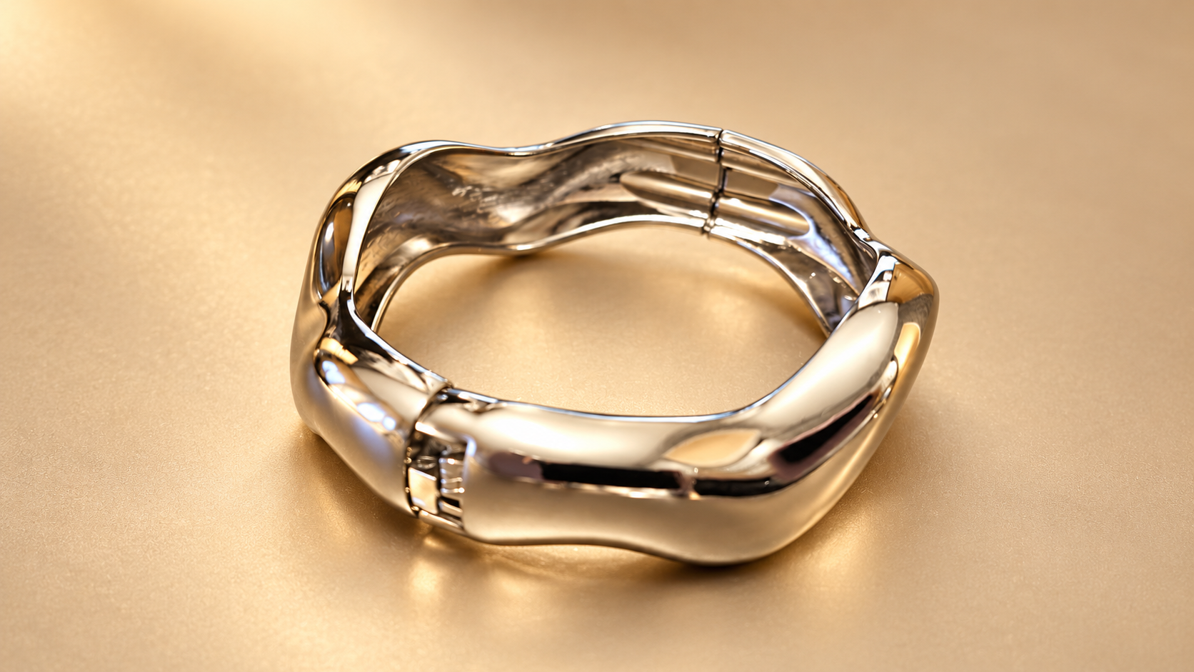 Bracelet Sillage Ondulé Argenté — Bracelet argenté orienté de biais, laissant voir l'articulation au premier plan, la surface intérieure et les courbes brillantes.