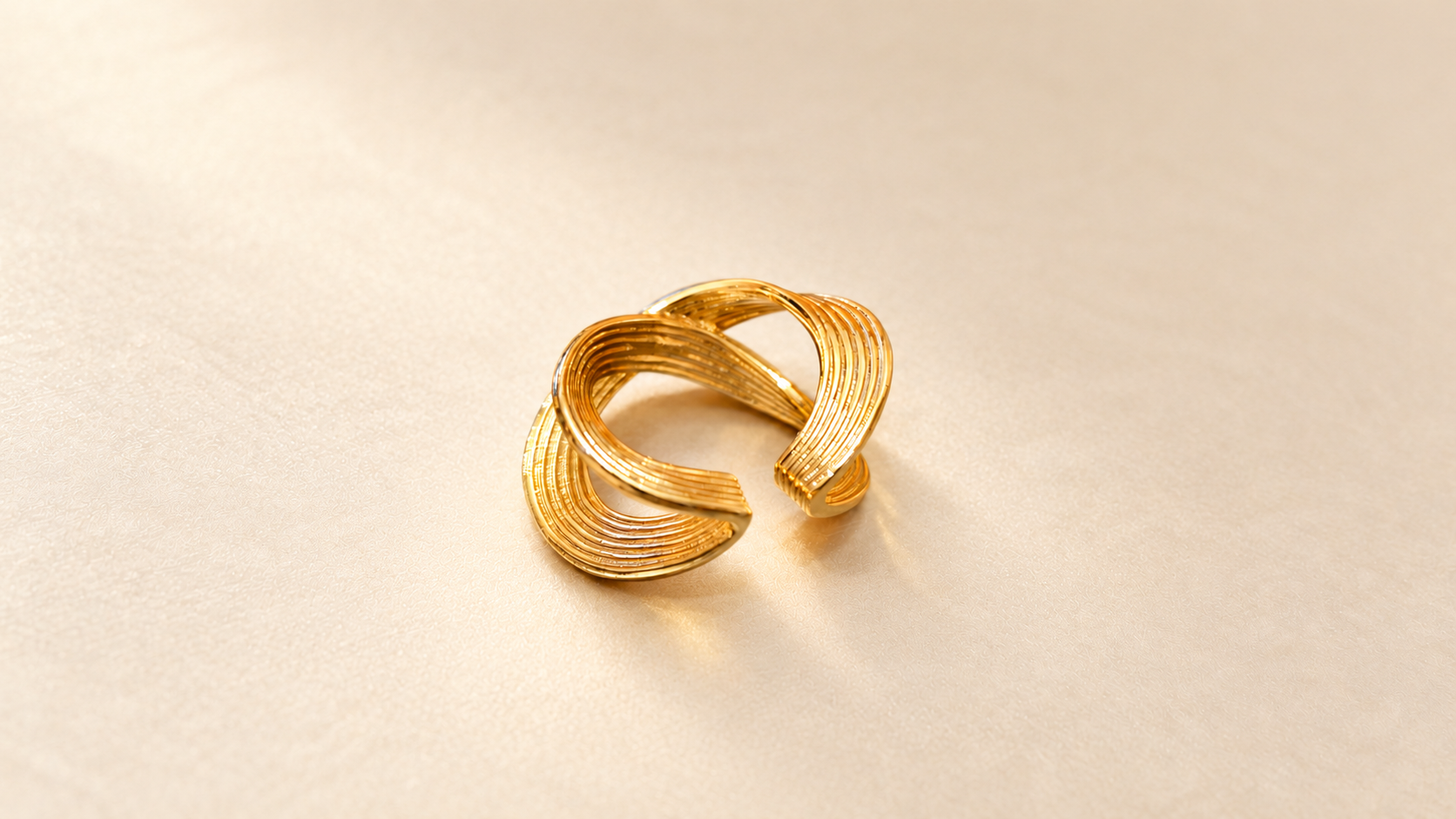 Bague Sillage Croisée Dorée — Bague dorée inclinée vue en plongée, ouverture intérieure et extrémités arrondies des bandes striées visibles.