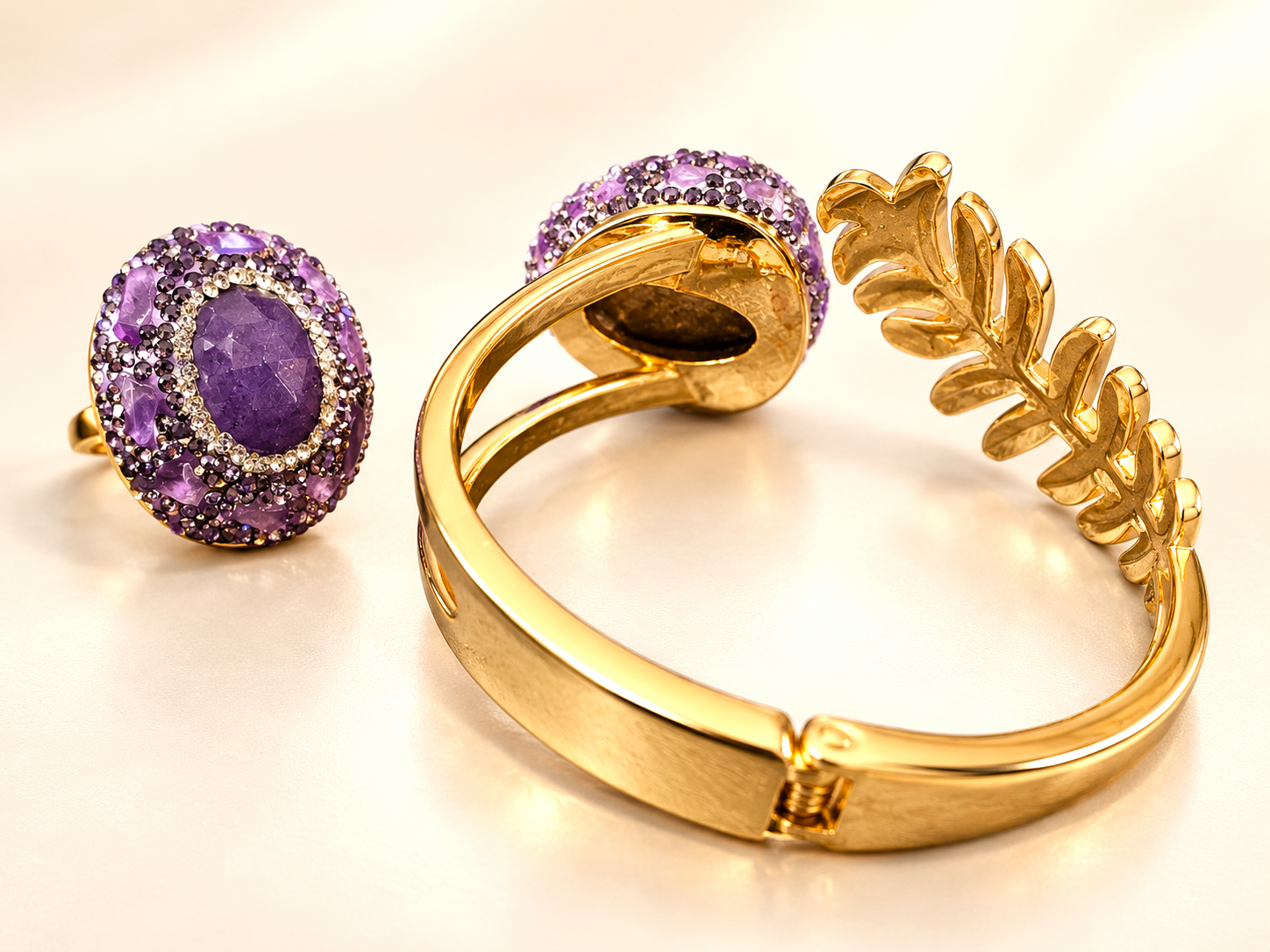 Parure Vesper Ovale Violette — Intérieur d’un bracelet doré au premier plan, articulation visible et revers du motif feuillage, avec une bague ovale violette à gauche.