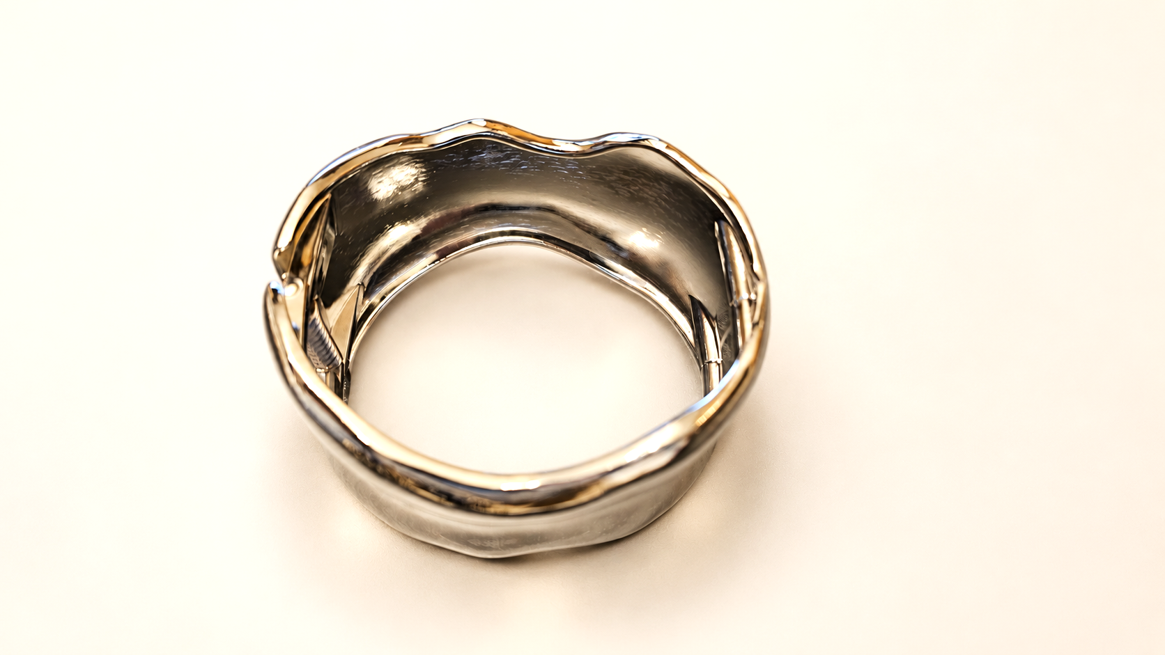 Bracelet Manchette Rivage Argenté — Manchette argentée vue de dessus, ouverture centrale arrondie et contours irréguliers soulignés de reflets chauds.