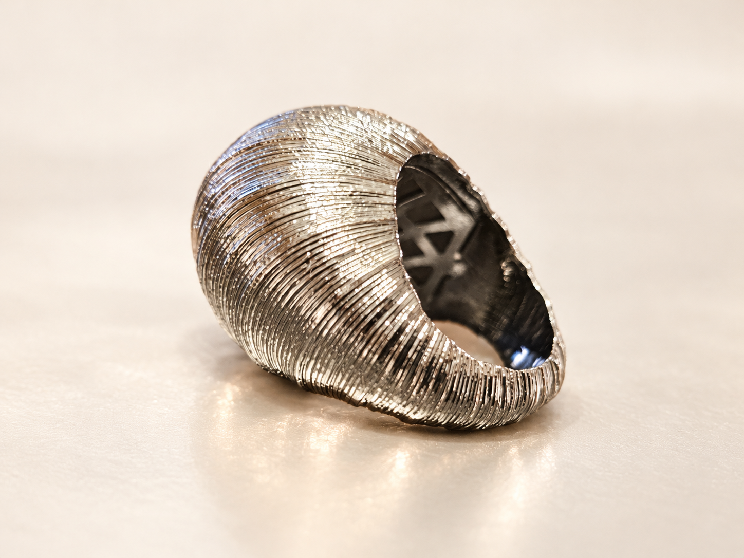 Bague Sillage Bombée Argentée — Bague argentée inclinée de trois-quarts, montrant le volume strié et une partie de l’intérieur ajouré.