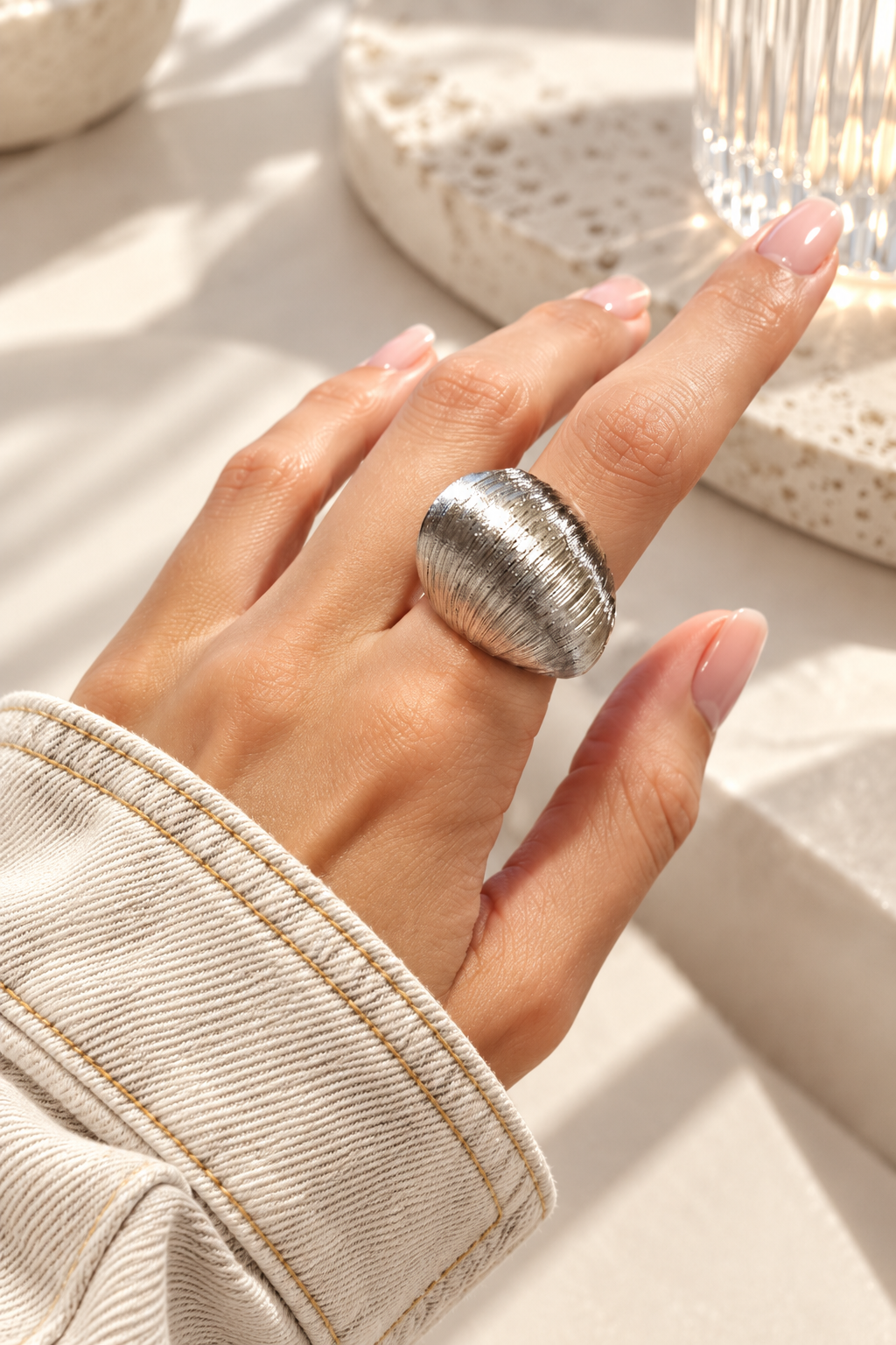 Bague Sillage Bombée Argentée — Bague argentée portée à la main, avec large dessus bombé et fines stries éclairées par une lumière vive.