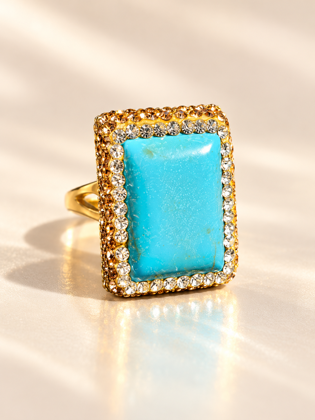 Bague Horizon Rectangle Bleu — Bague vue presque de face, cabochon rectangulaire bleu moucheté entouré d’éléments brillants clairs et champagne sur une monture dorée.