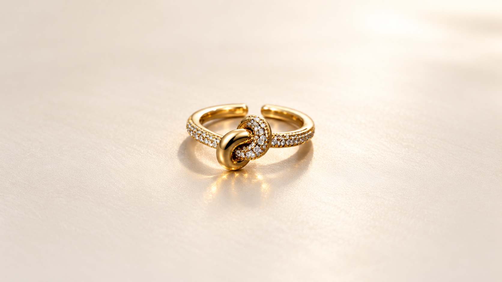 Bague Complicité Nouée | Dorés — Bague dorée sur fond clair, avec deux boucles entrelacées de face, l’une lisse et l’autre ornée de petits éléments brillants.